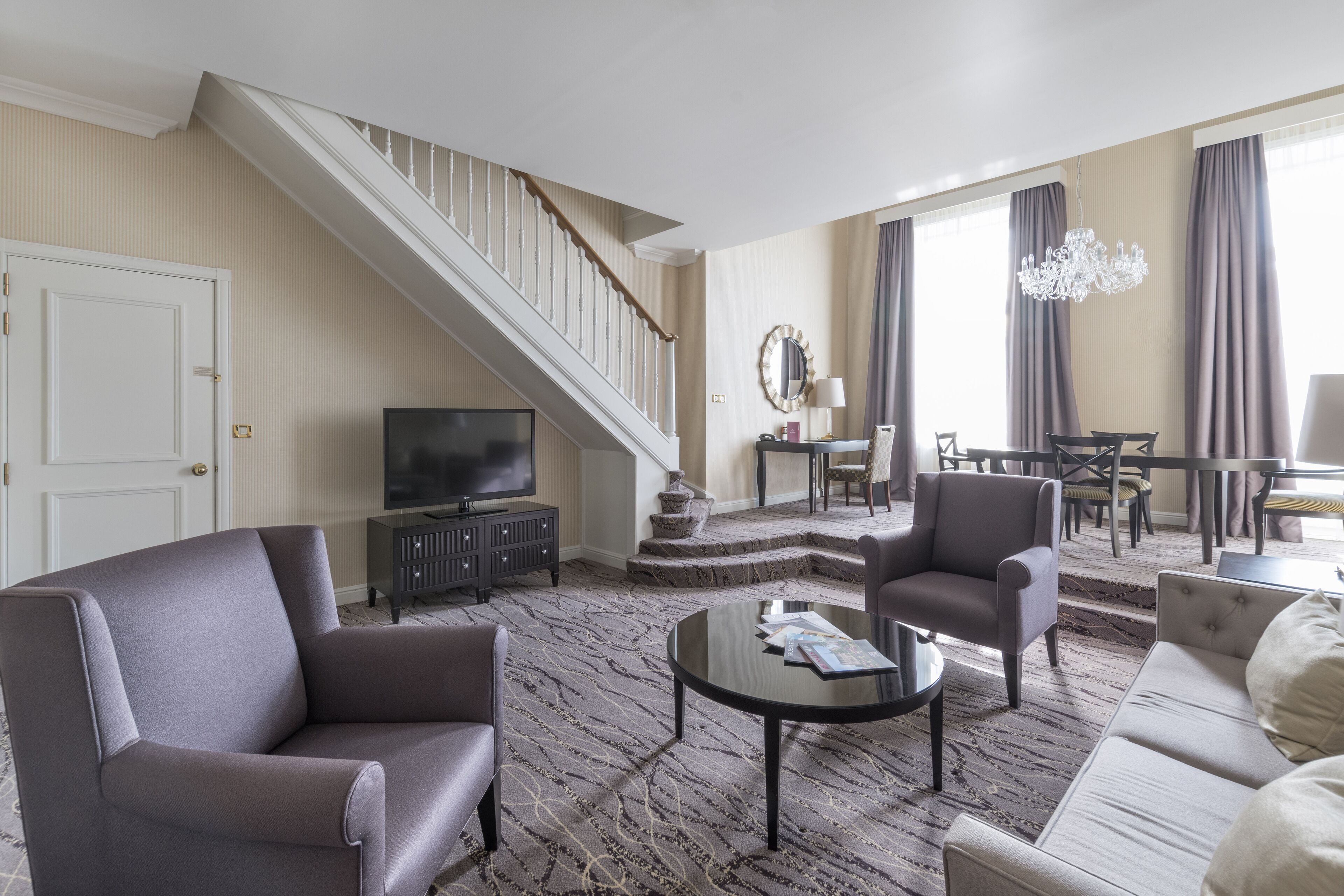 A modern living room with a staircase, a television, and a dining area.