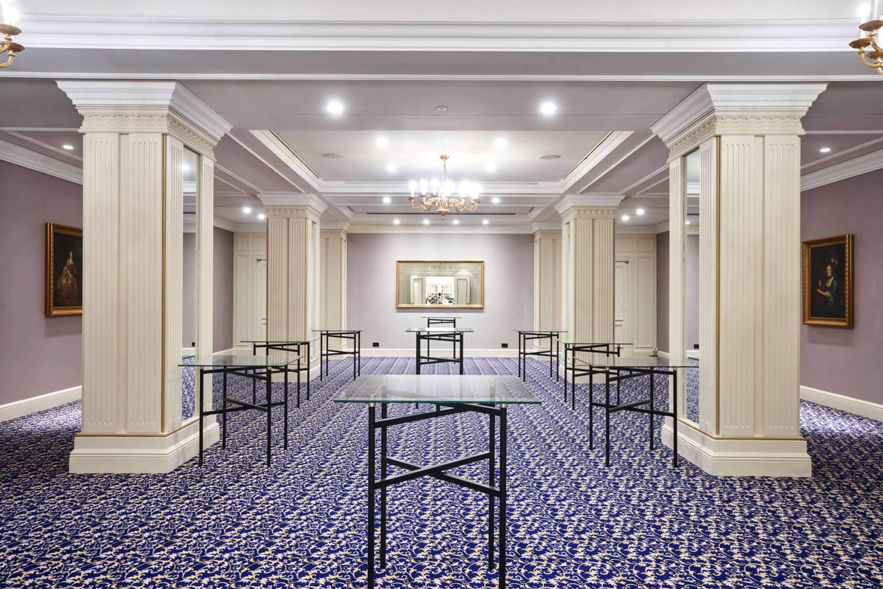 Una sala de conferencias con una mesa de vidrio, sillas de metal negro y una alfombra estampada.