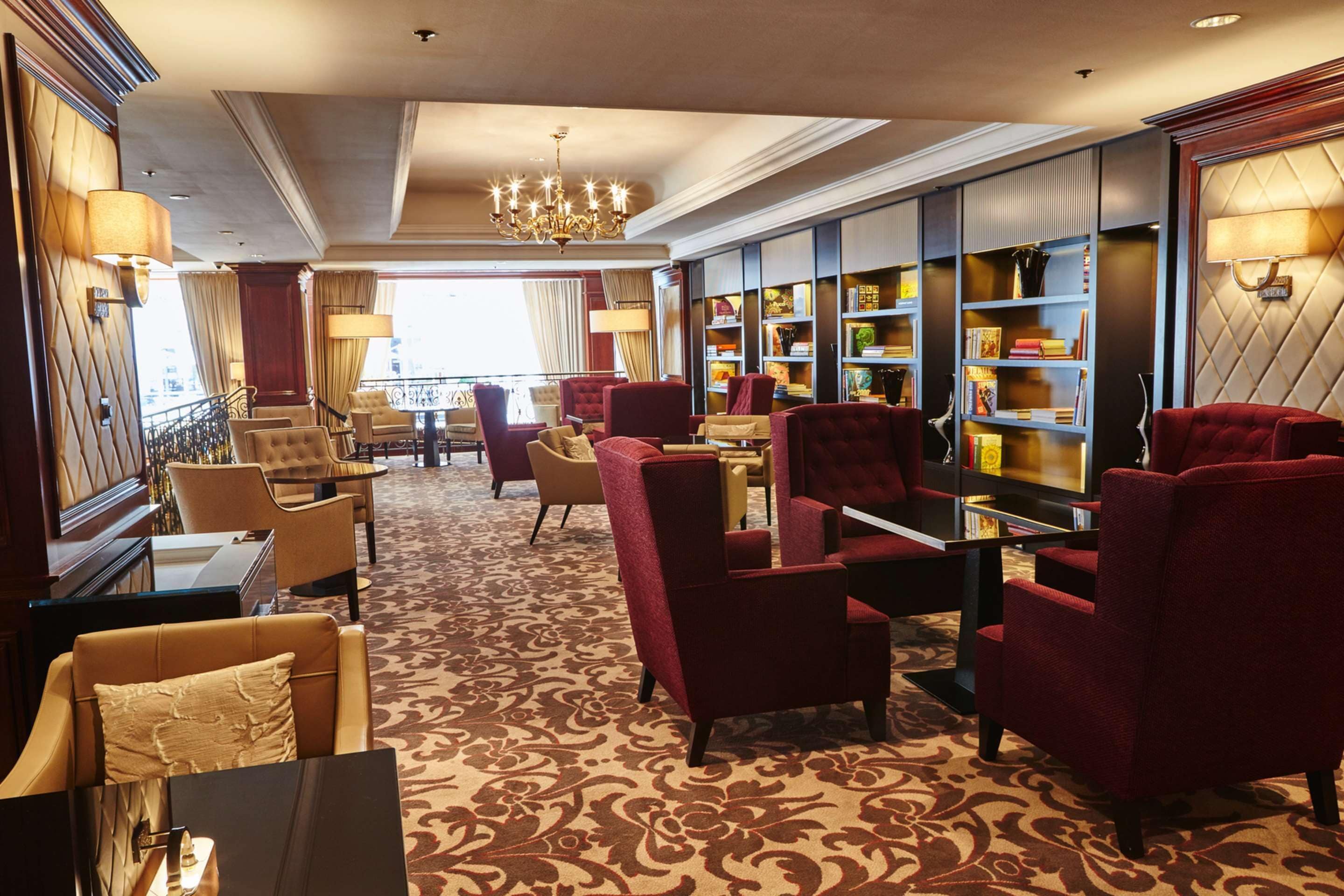 Een hotel lobby met rode bekleden stoelen, een kamerbreed tapijt, een kroonluchter en boekenkasten met boeken.