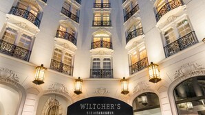 Imponente entrada de hotel con balcones ornamentales, un cartel llamativo y una fachada bien iluminada.
