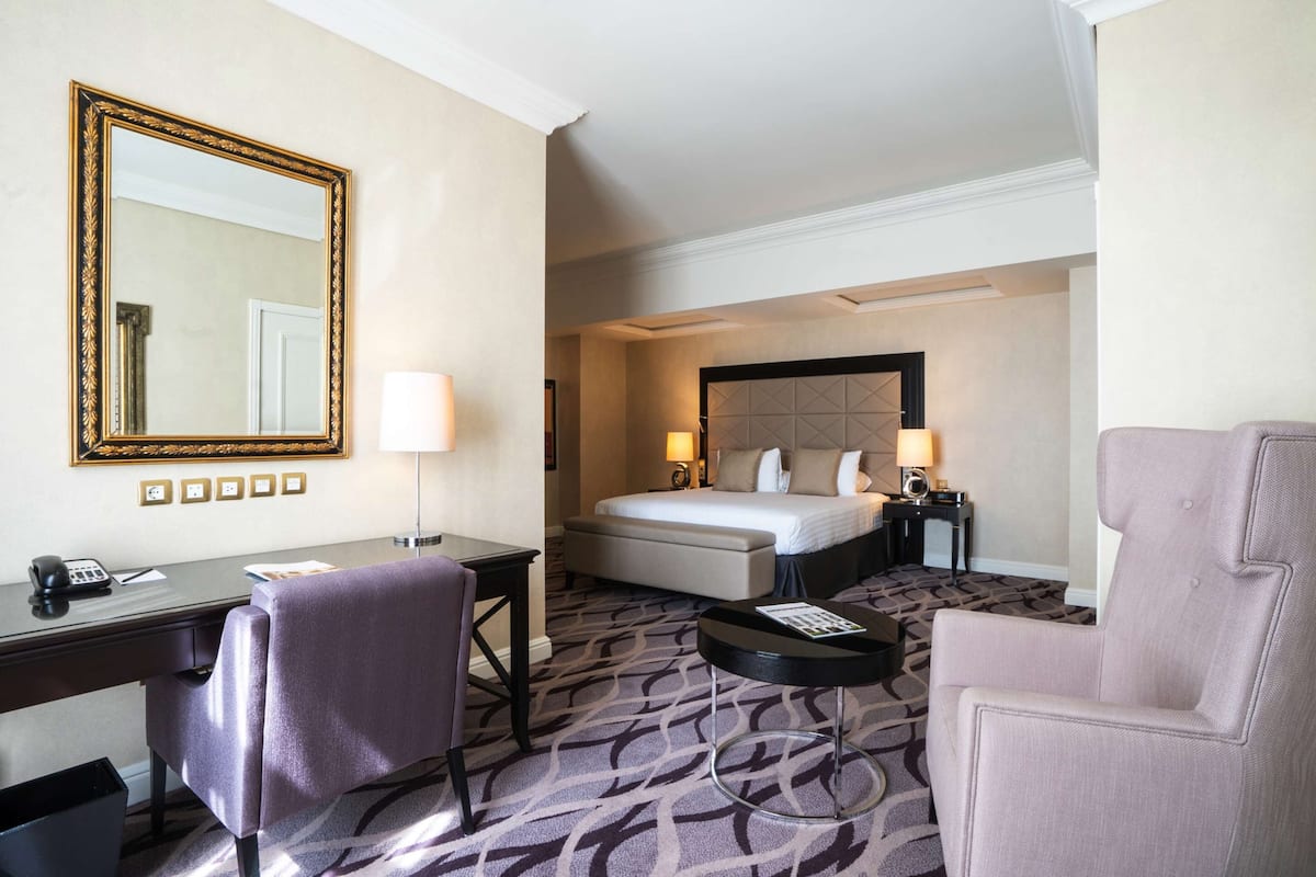 A hotel room with a bed, desk, chair, and a large mirror.
