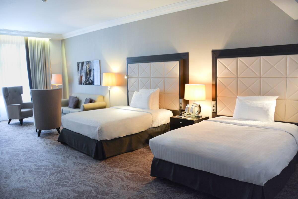 A hotel room with two beds, a sofa, a chair, and a lamp.