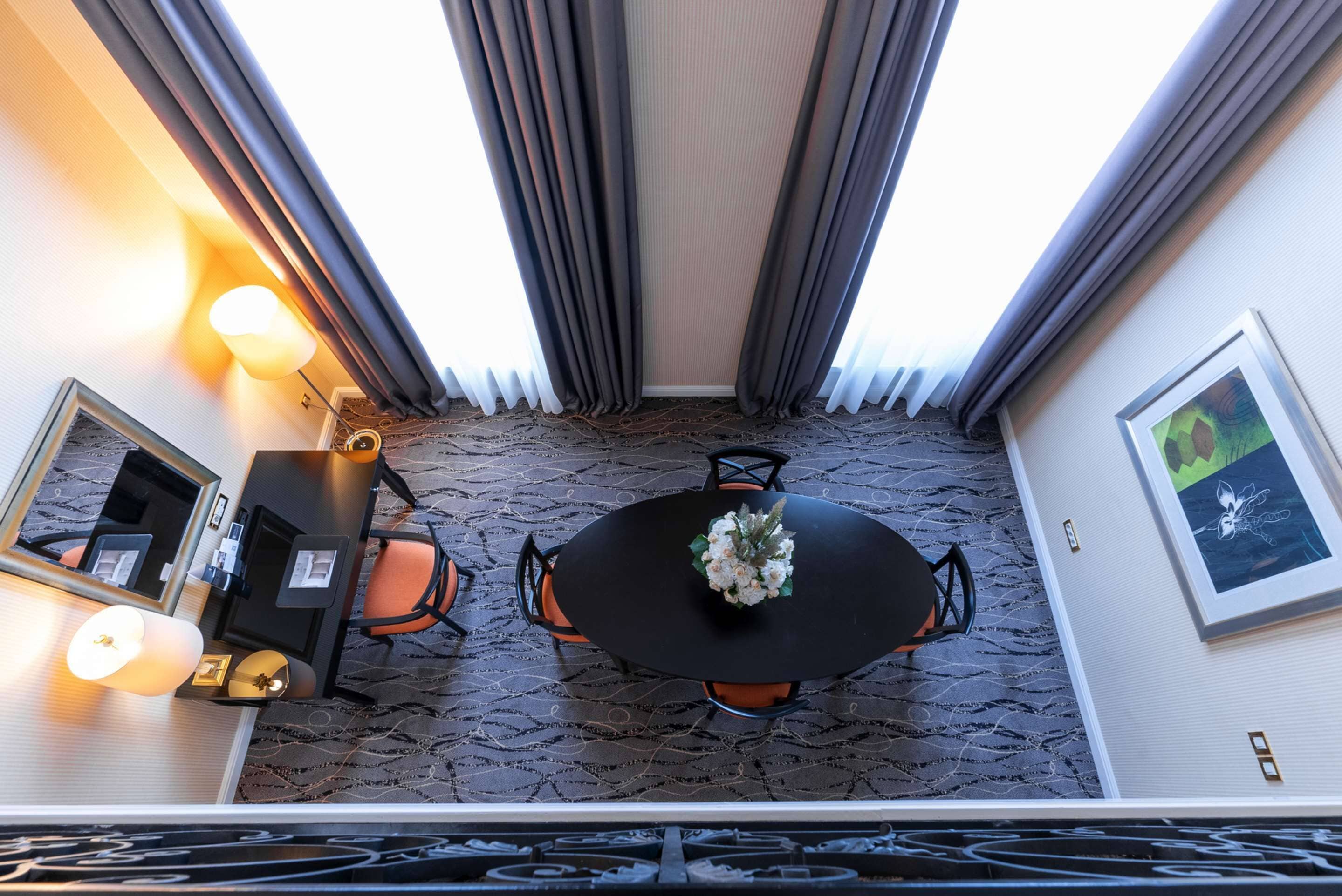Hotelkamer met een ronde tafel, twee stoelen, een bureau met stoel, een spiegel en een lijst met een afbeelding aan de muur.