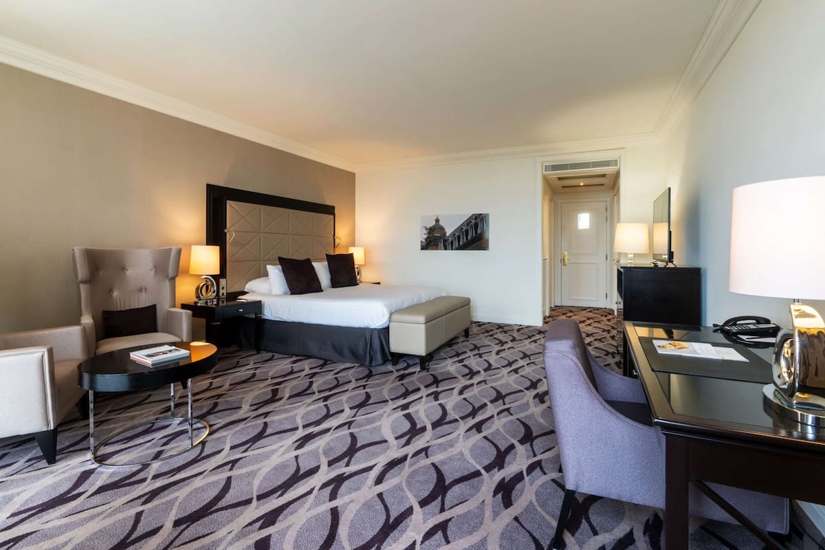 A hotel room with a bed, a desk, a chair, a sofa, and a television.
