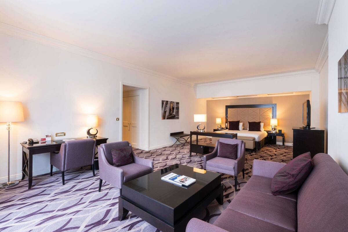A hotel room with a living area, a bed, a desk, and a coffee table.