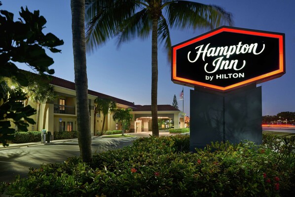 A Hampton Inn by Hilton sign with a well-lit entrance and a landscaped garden in front.