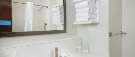 Un baño moderno con un espejo grande, lavamanos blanco y espacio para toallas.