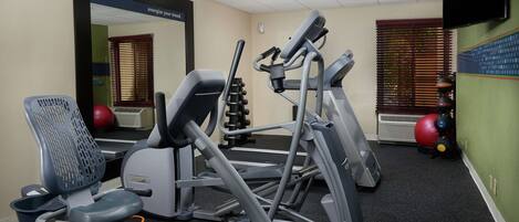 A gym with exercise equipment, a mirror, and a wall-mounted TV.
