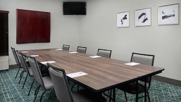 Una sala de conferencias con una larga mesa, sillas, un televisor de pantalla plana y cuadros en la pared.