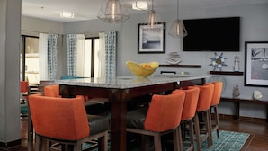 Un comedor moderno con una isla central, taburetes de bar y un televisor de pantalla plana montado en la pared.