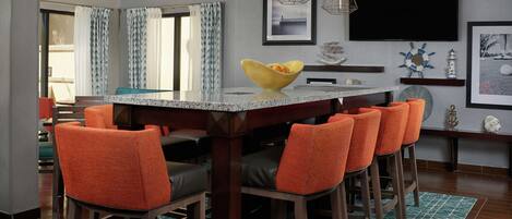 A modern dining area with a central island, bar stools, and a flat-screen TV mounted on the wall.