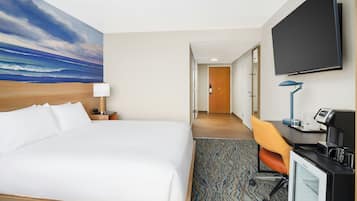 A hotel room with a large bed, a desk with a computer, a flat-screen TV, and a painting of a beach scene.