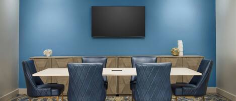 A dining area with a blue wall, a flat-screen TV, and a patterned carpet.