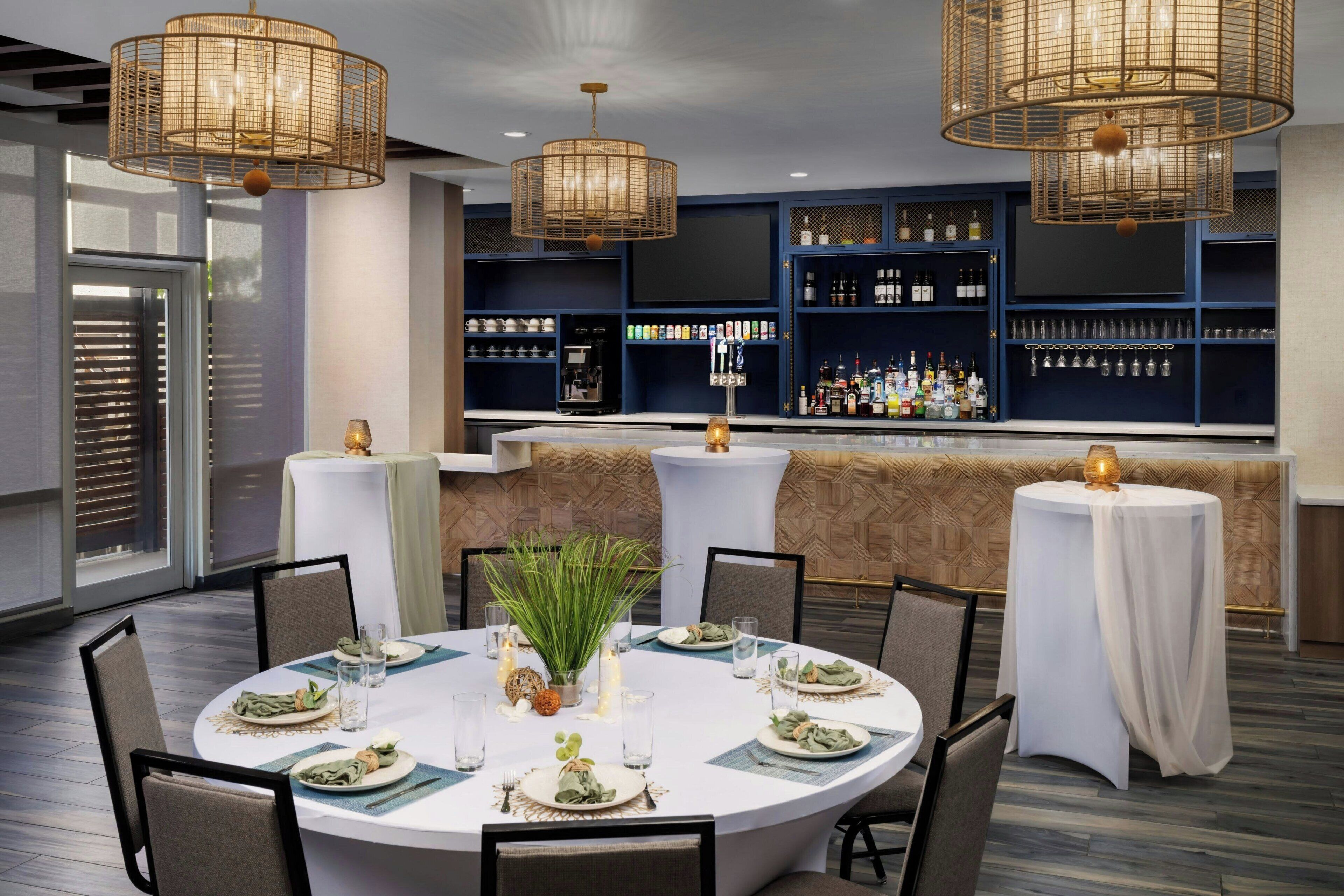 A dining area with round tables, chairs, and a bar with shelves of bottles.