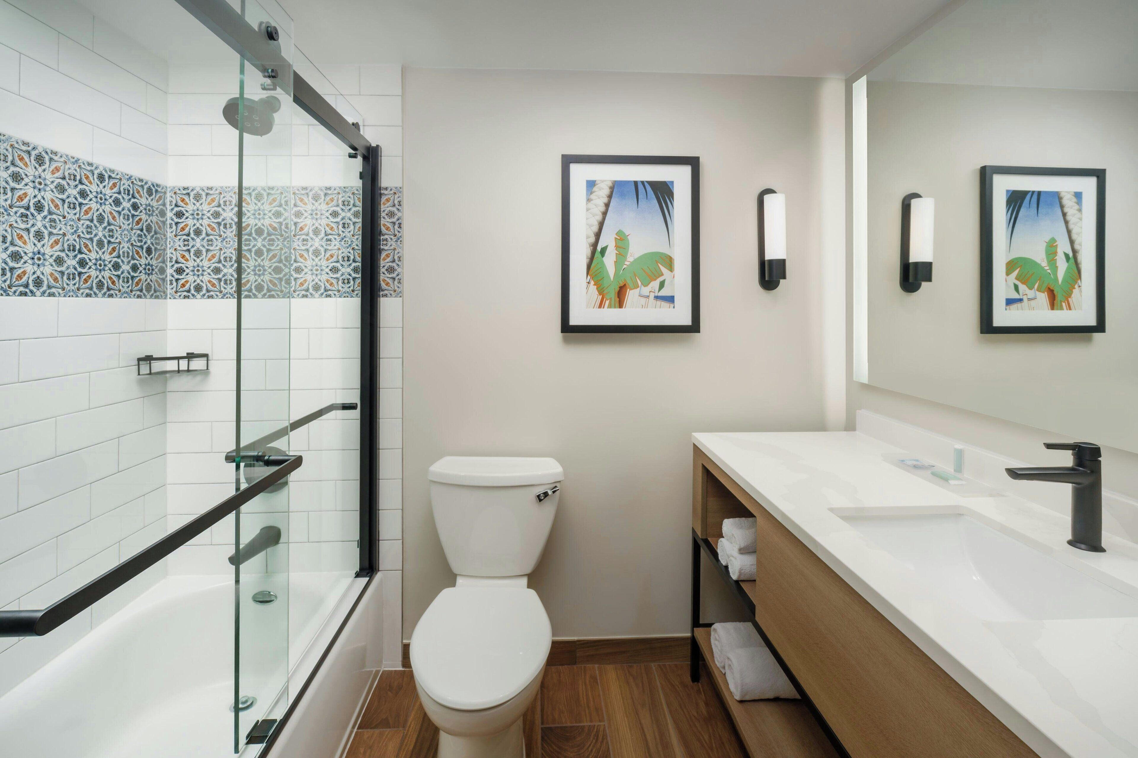 A modern bathroom with a glass-enclosed shower, a white toilet, and a wooden vanity with a sink and towel rack.