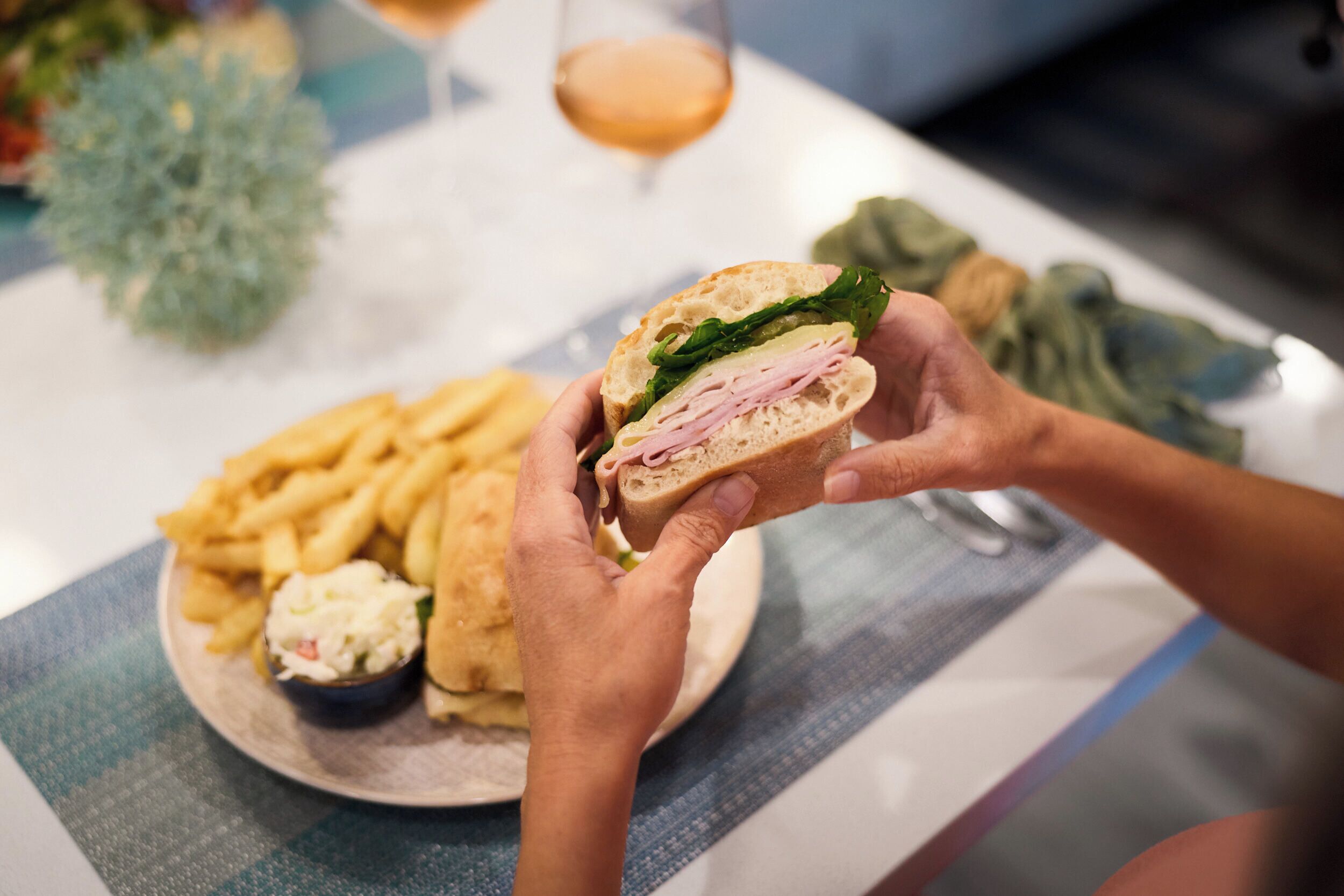 A person holding a sandwich with a side of fries and a small bowl of coleslaw.