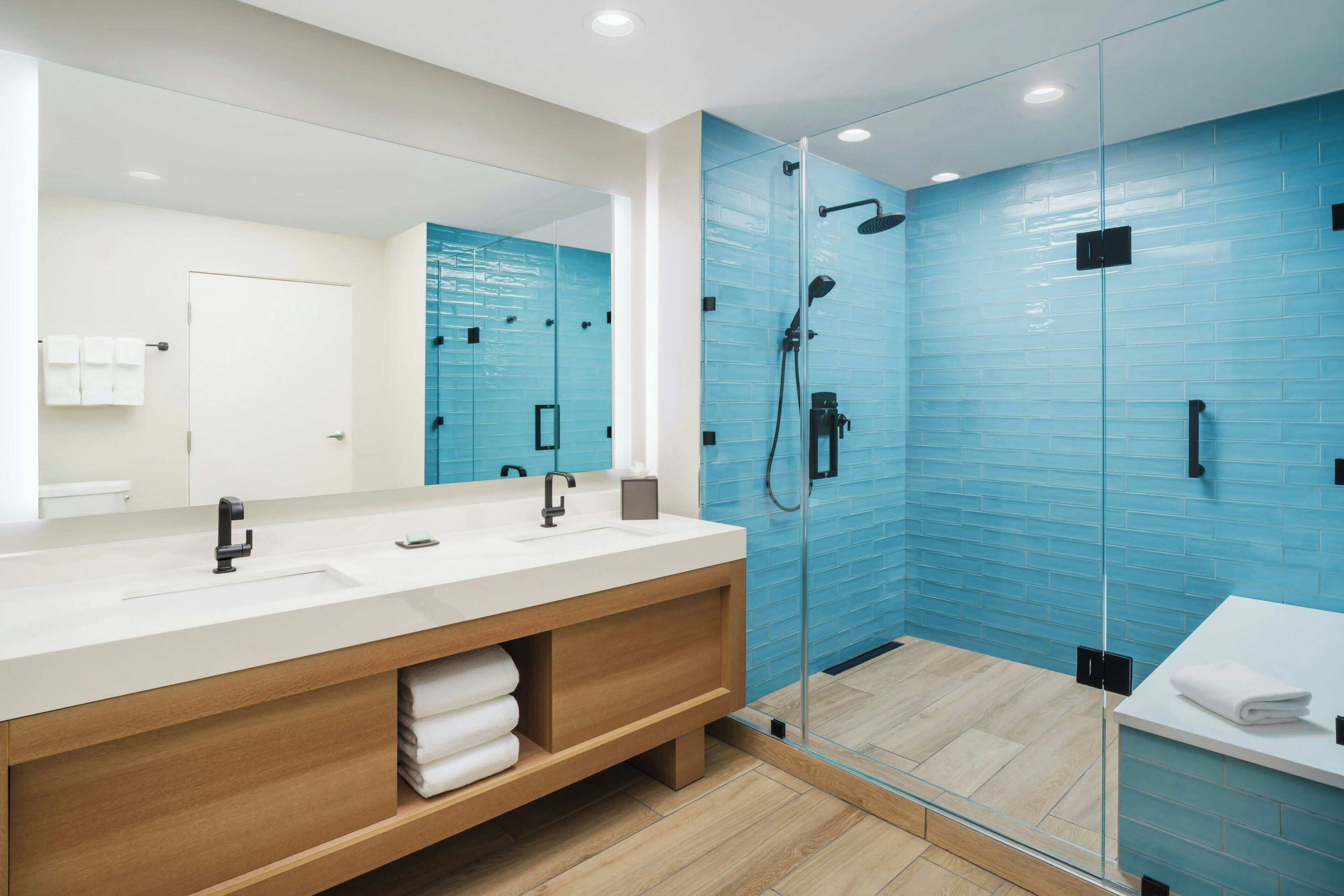 Un baño moderno con ducha de vidrio, tocador de madera y un espejo grande.