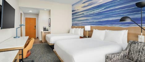 A hotel room with two beds, a desk, a chair, a TV, and a painting of a sky.