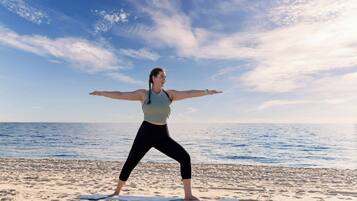 A person performing a yoga pose on a mat on a beach with the sea and sky in the background.