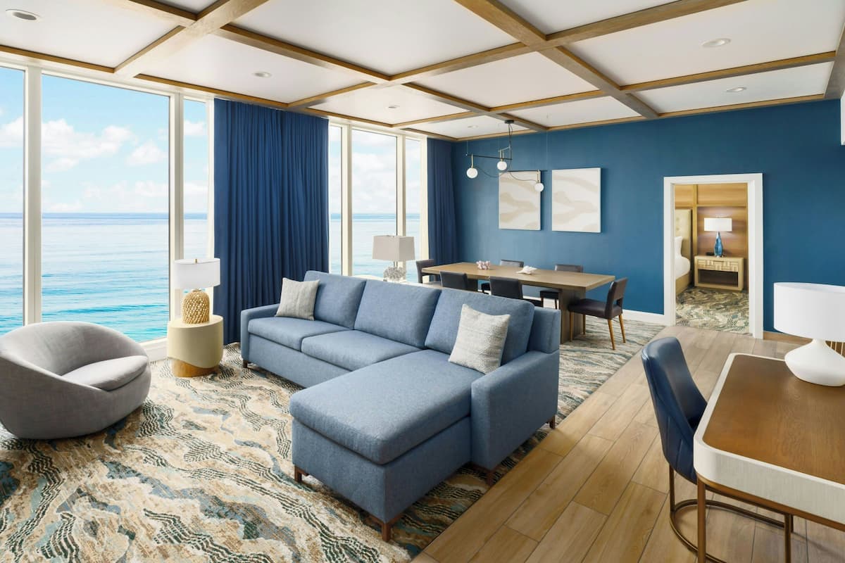 Ein modernes Wohnzimmer mit einem großen blauen Sofa, einem Esstisch und Blick auf den Ozean.