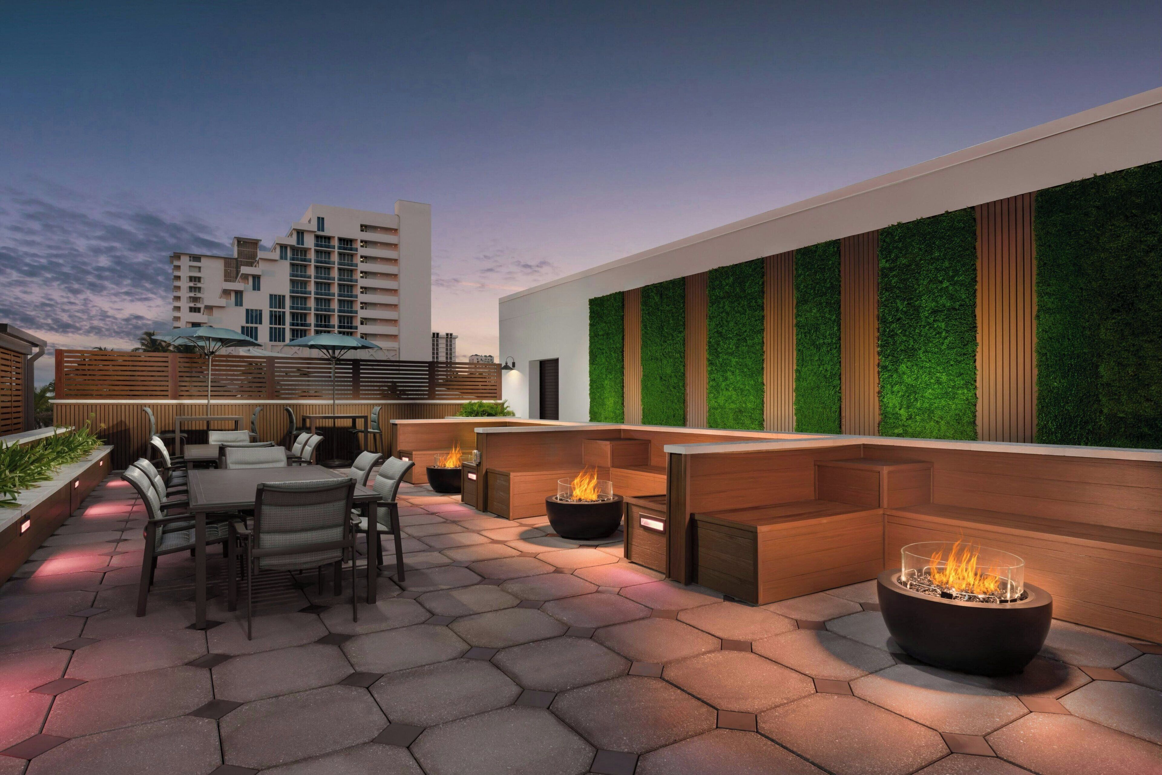 An outdoor patio area with hexagonal tiles, wooden seating, and fire pits.