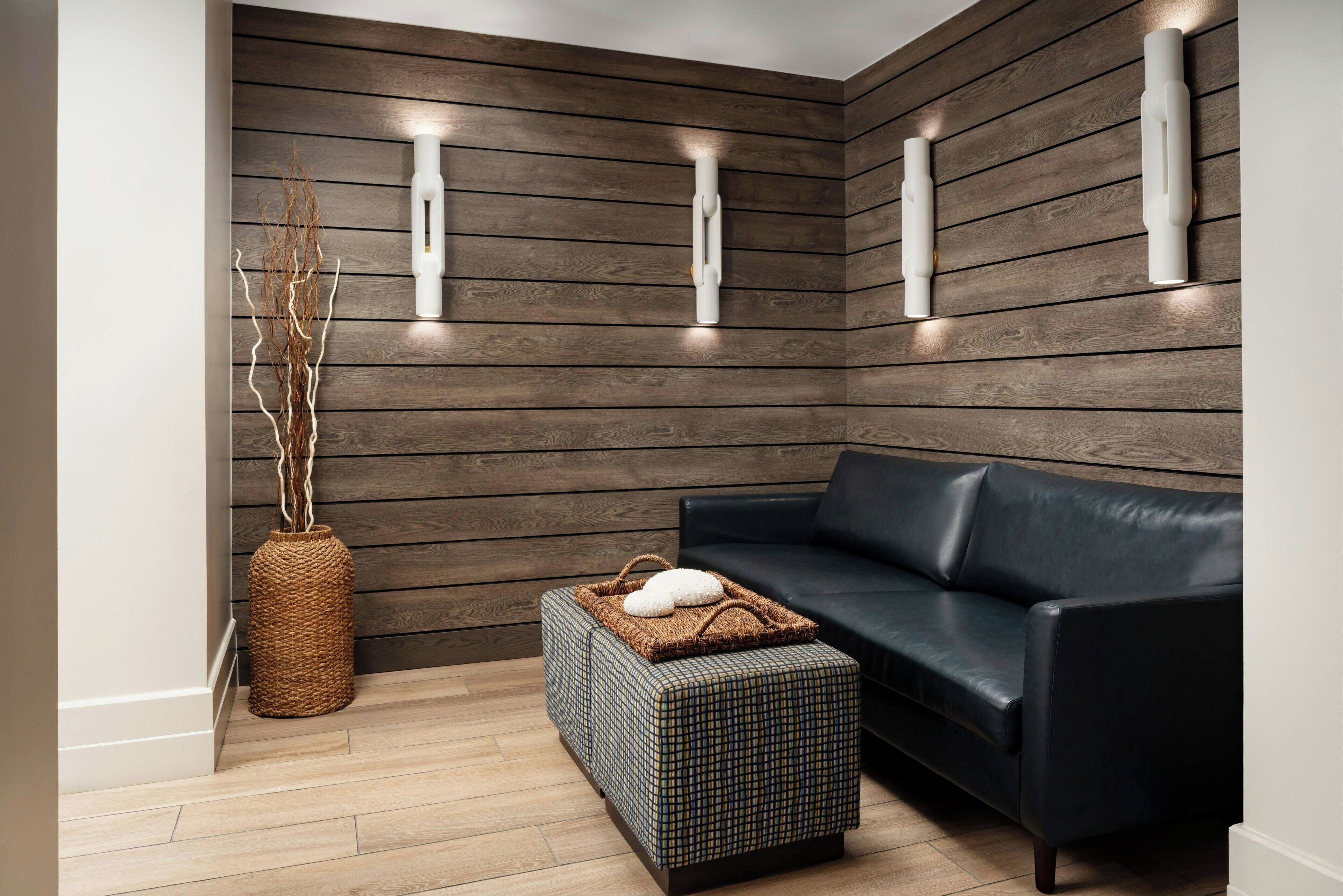 Una sala de estar moderna con una pared de madera marrón oscuro, un sofá de cuero negro, un pouf tejido y un jarrón de mimbre.