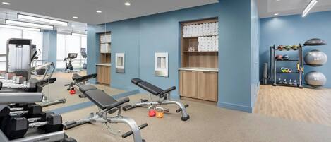 Un gimnasio moderno con equipo de ejercicio, una banca y un estante de pared con pesas.