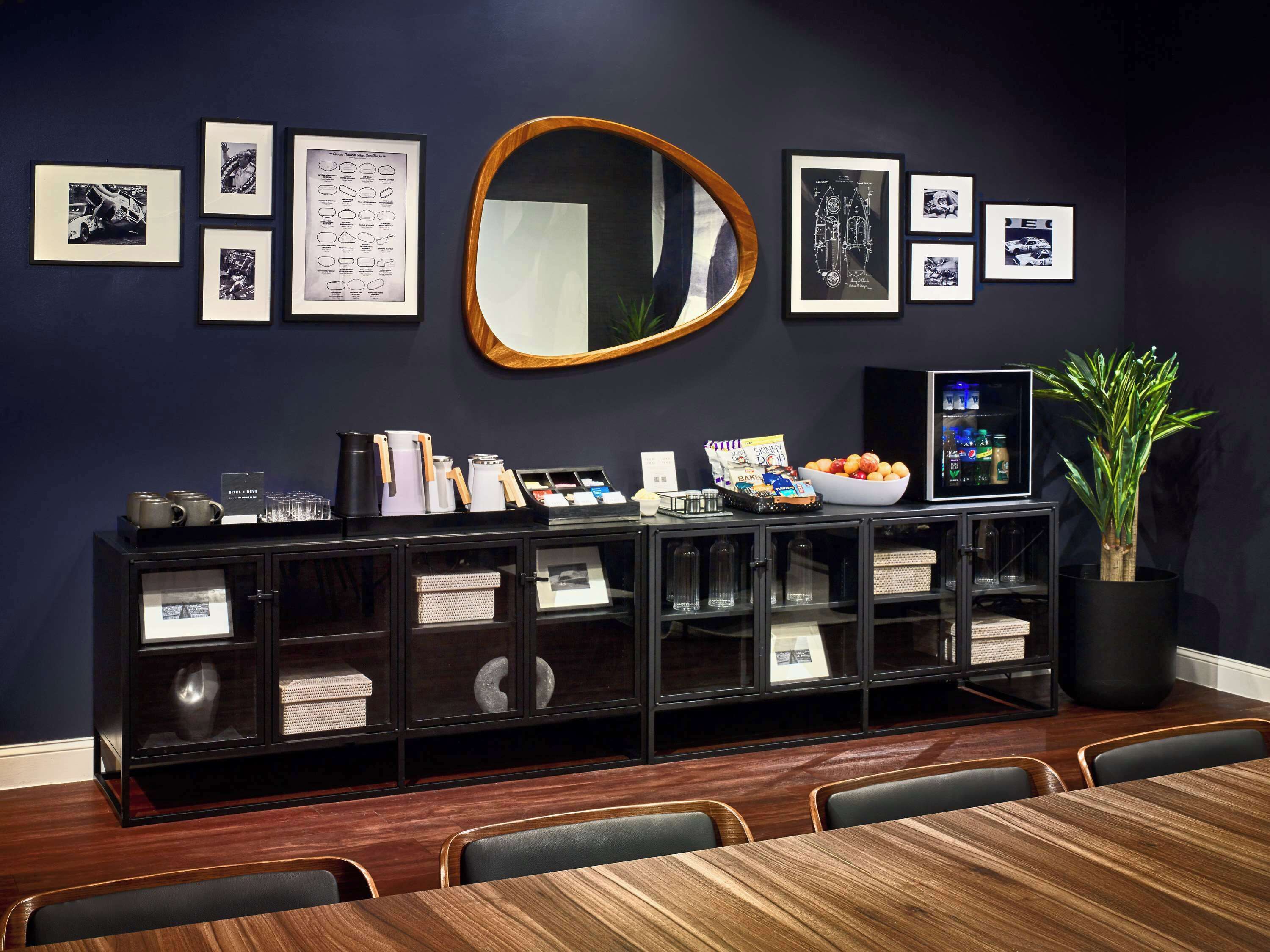 A conference room with a dark blue wall, a wooden conference table, and a black cabinet with glass doors.