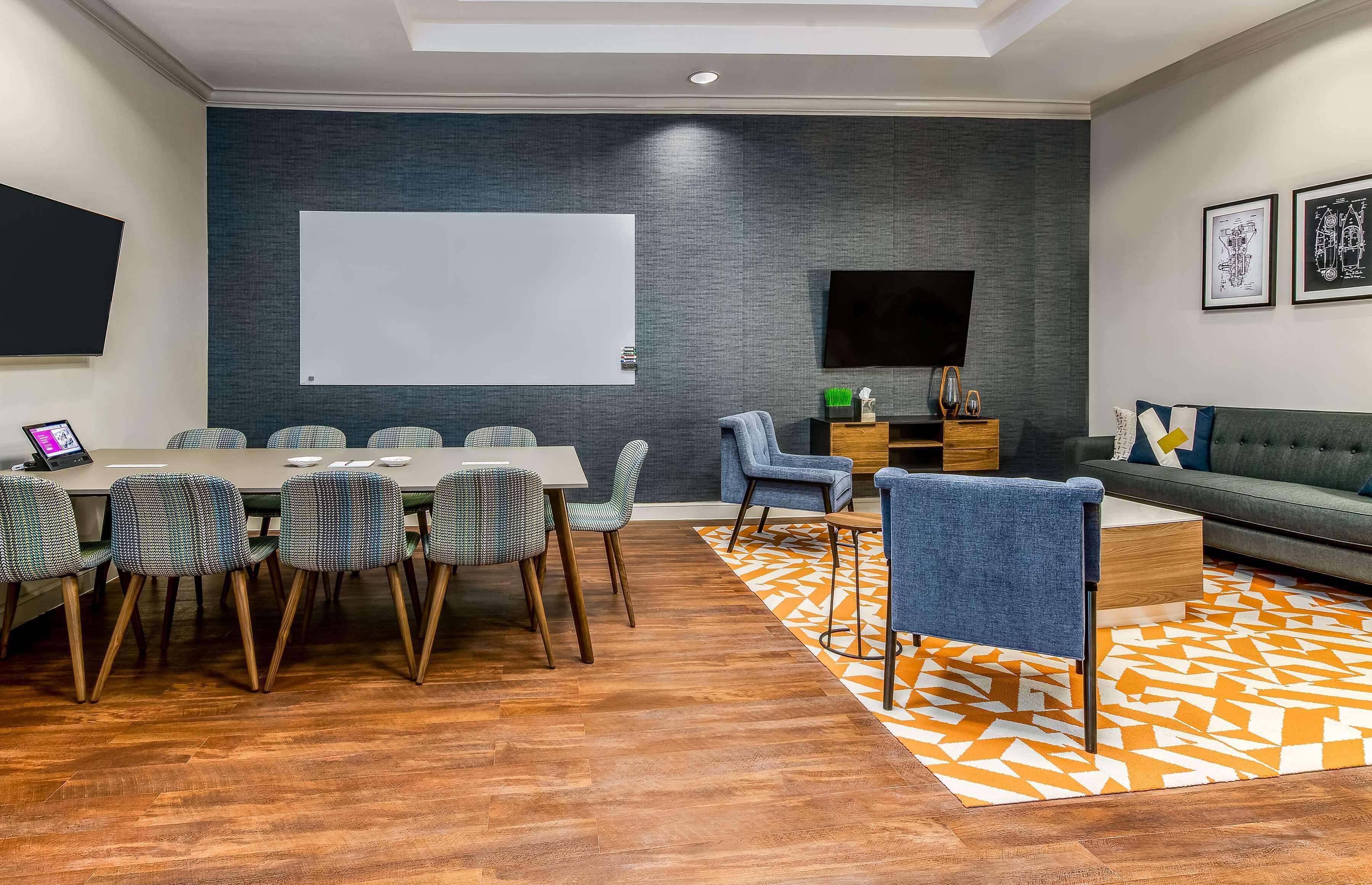A modern meeting room with a large table, chairs, a sofa, and a TV screen.