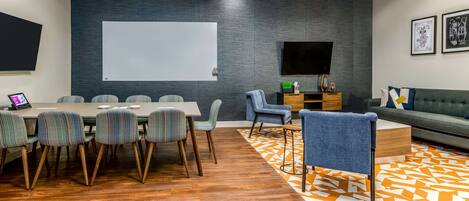A modern meeting room with a large table, chairs, a sofa, and a TV screen.