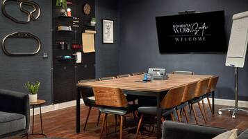 A modern conference room with a wooden table, black chairs, and a blackboard with 'SONES' and 'WELCOME' written on it.