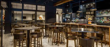 A modern bar area with multiple seating options, including bar stools and tables, and a well-stocked bar counter.