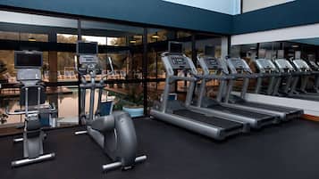 A modern gym with treadmills, an elliptical, and a rowing machine, featuring large windows and a pool view.