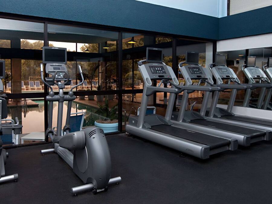 A modern gym with treadmills, an elliptical, and a rowing machine, featuring large windows and a pool view.