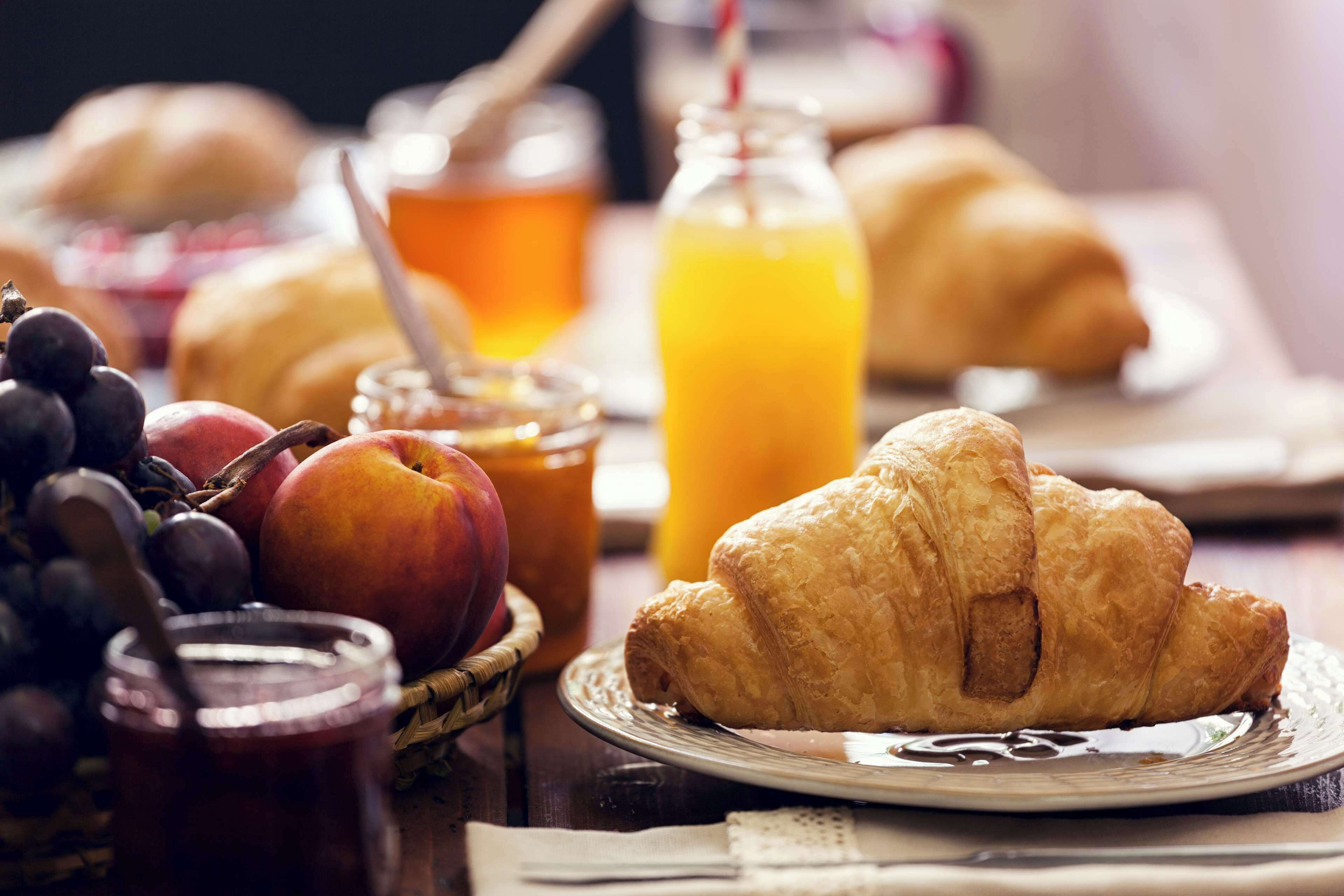 Ein Frühstückstisch mit Croissants, Äpfeln, Trauben und einem Glas Orangensaft.