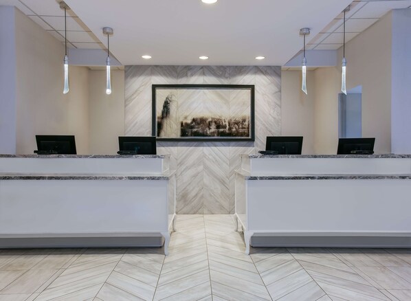 A reception area with two reception desks, a large framed artwork on the wall, and a herringbone patterned floor. - Sonesta Charlotte Lower South End (Charlotte)