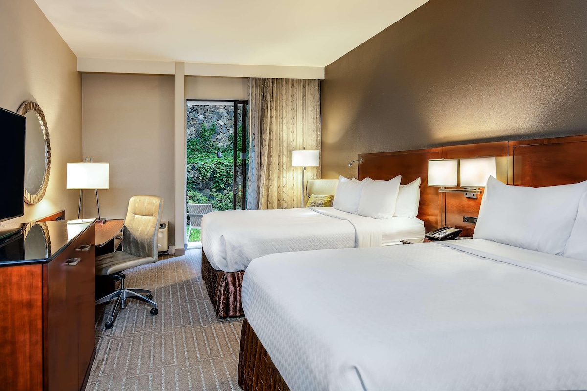 Een hotelkamer met twee bedden, een bureau met stoel, een televisie en een raam met gordijnen.