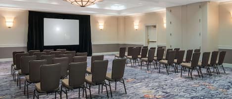 A conference room with rows of chairs, a large screen, and wall sconces.