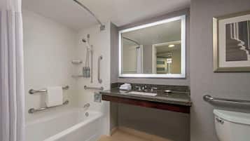 A modern bathroom with a bathtub, shower, and toilet. It includes grab bars and a vanity with a mirror.