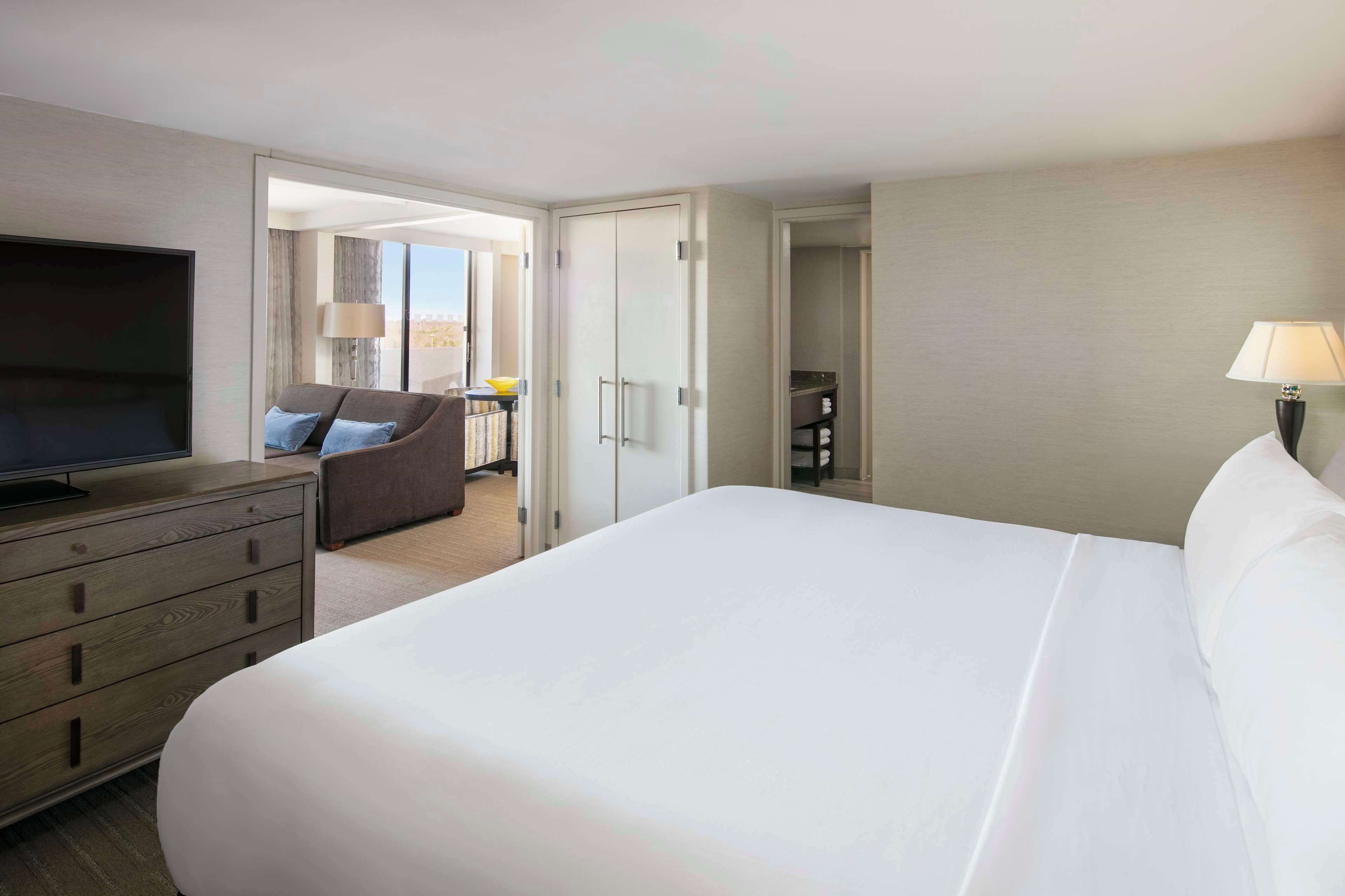 A hotel room with a large bed, a TV, a desk with a lamp, and a view of the city through the window.