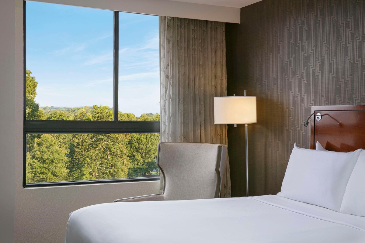 Een hotelkamer met een groot raam, een bed, een stoel en een lamp.