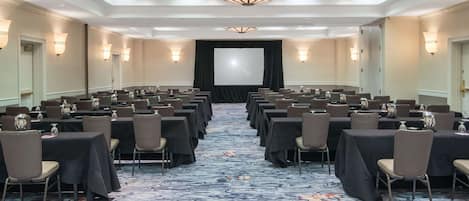 A conference room with rows of tables and chairs, a large screen at the front, and a patterned carpet.