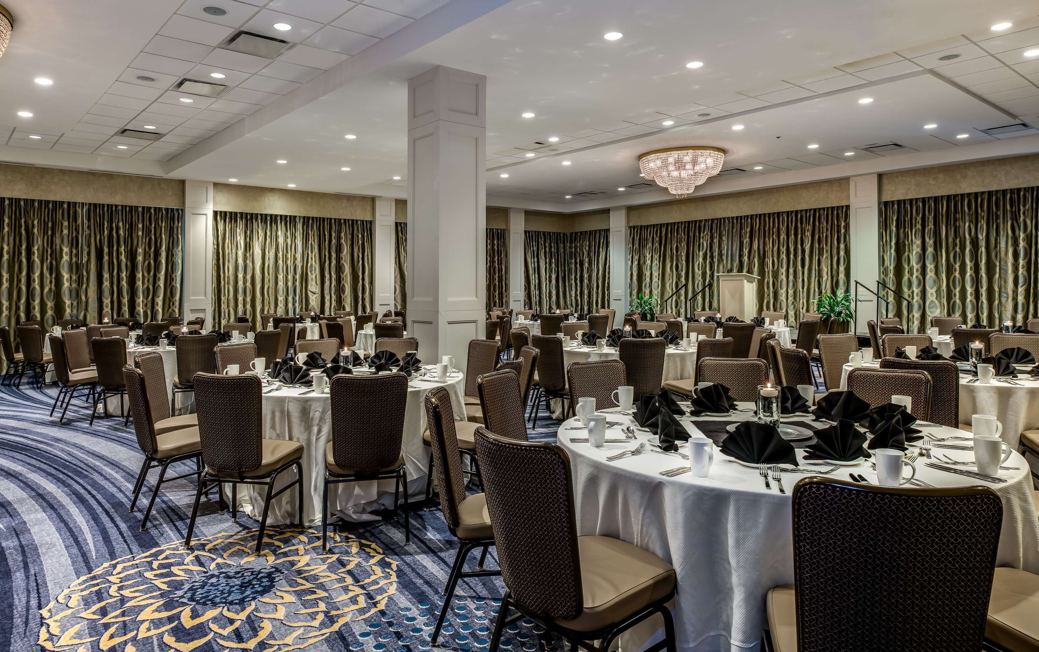 A large banquet hall with round tables, chairs, and a patterned carpet.
