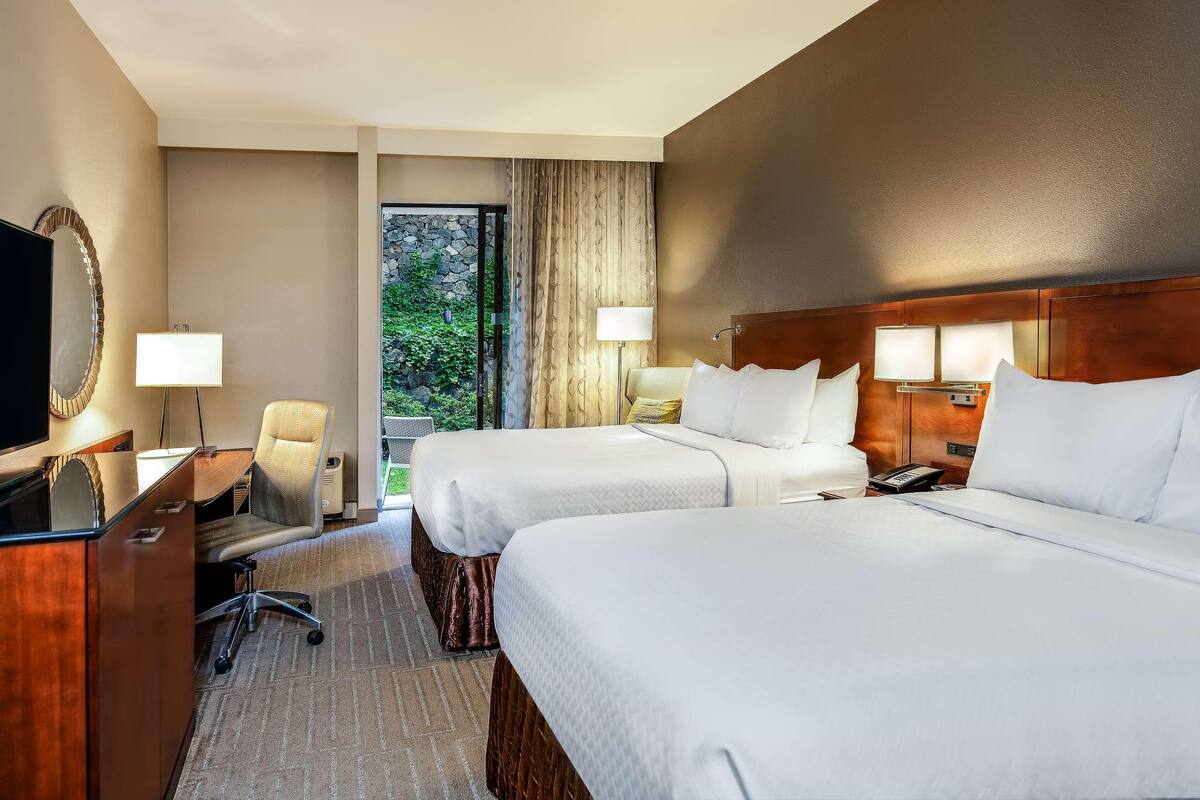 A hotel room with two beds, a desk with a chair, a TV, and a window with curtains.