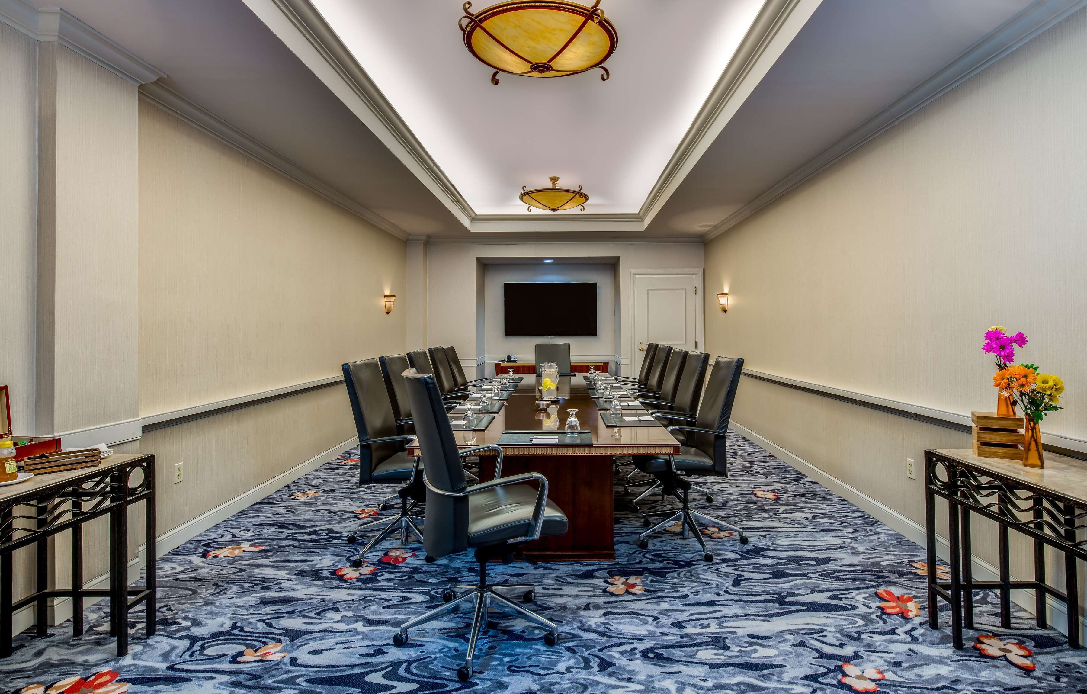 Un salón de conferencias con una larga mesa, sillas, un televisor de pantalla plana y una alfombra con motivos florales.