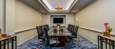A conference room with a long table, chairs, a flat-screen TV, and a floral carpet.