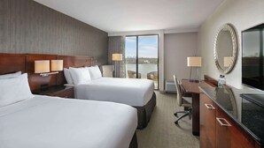 A hotel room with two beds, a desk, a chair, a TV, and a large window with a view. - Sonesta Charlotte Lower South End (Charlotte)