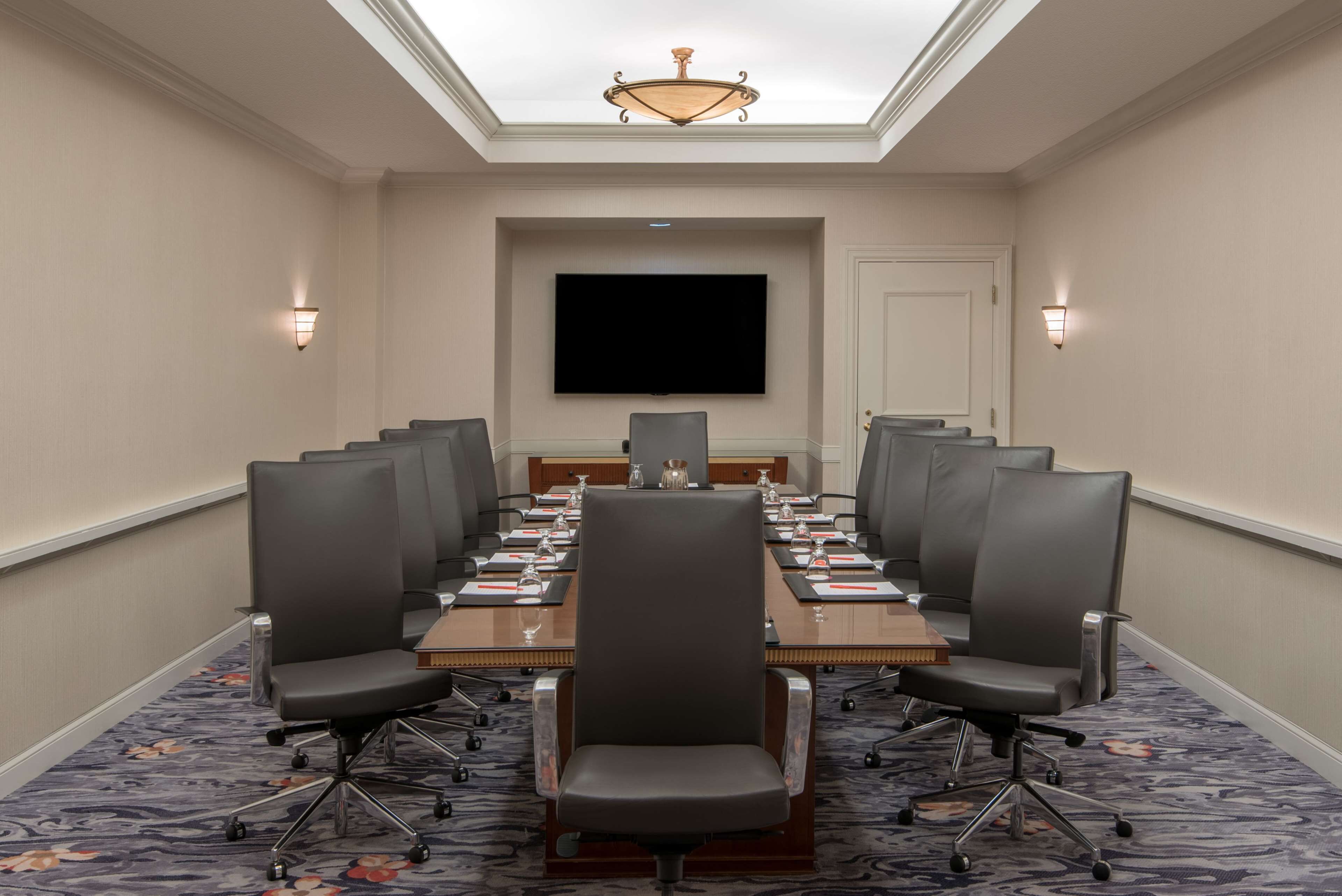 A conference room with a long table, chairs, a flat-screen TV, and a chandelier.