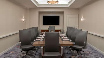 A conference room with a long table, chairs, a flat-screen TV, and a chandelier.