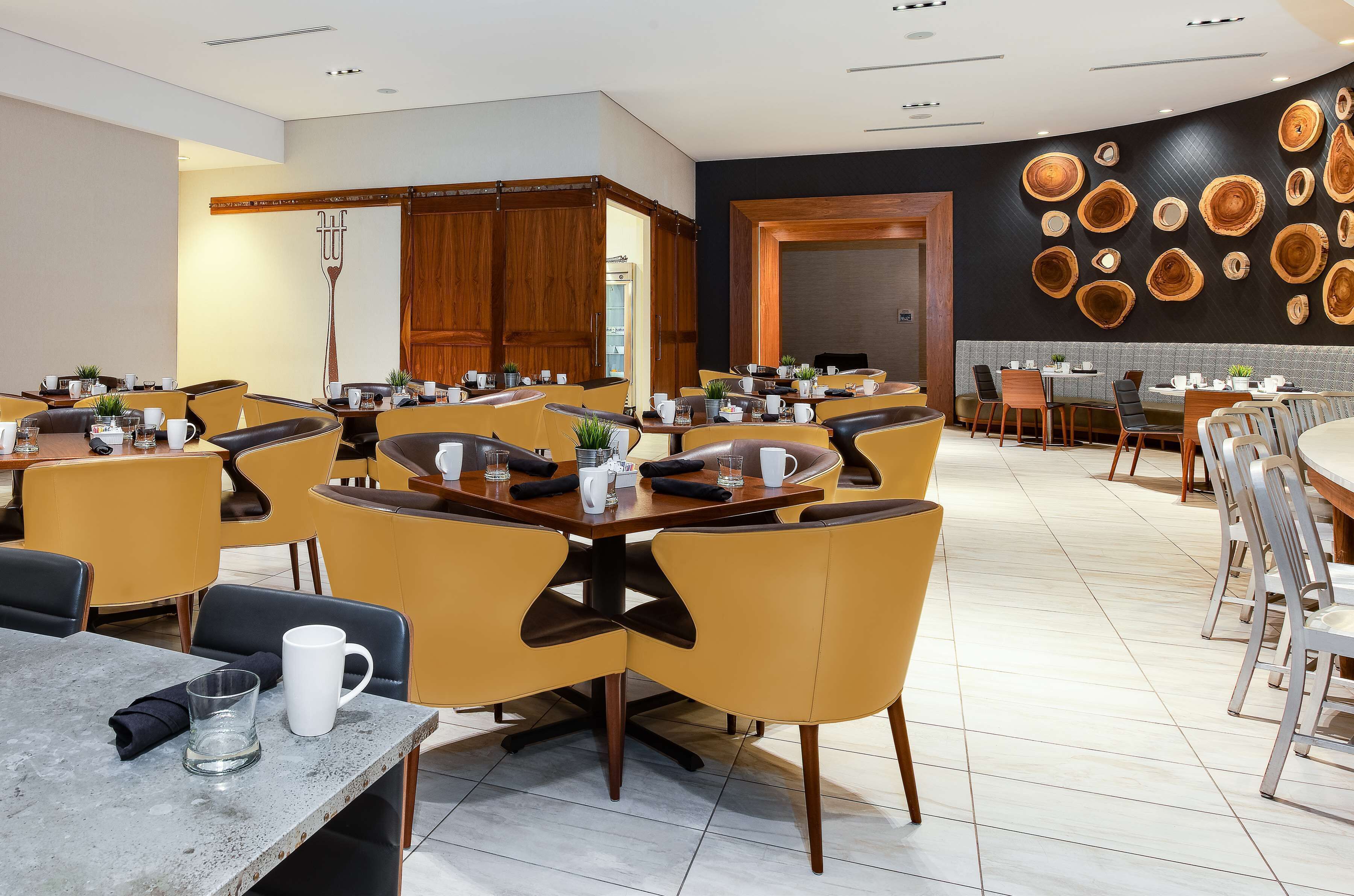 A modern dining area with multiple tables and chairs, wooden cabinets, and a wall decorated with circular wooden patterns.
